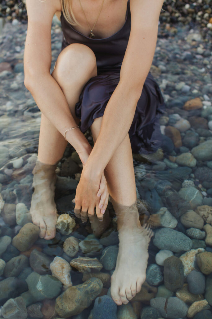 Woman sitting in a shallow rocky stream with her feet in the water